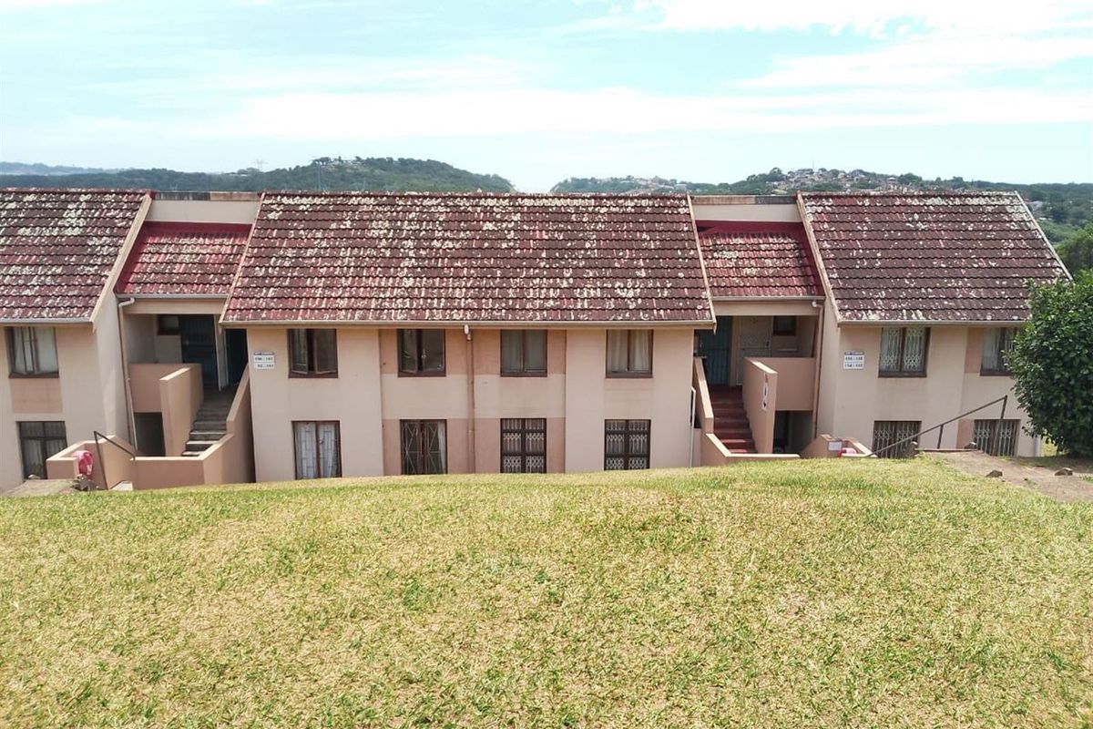 Rear view of a multi-unit apartment complex featuring a sloped lawn, tiled roofing, and external staircases providing access to the upper levels.