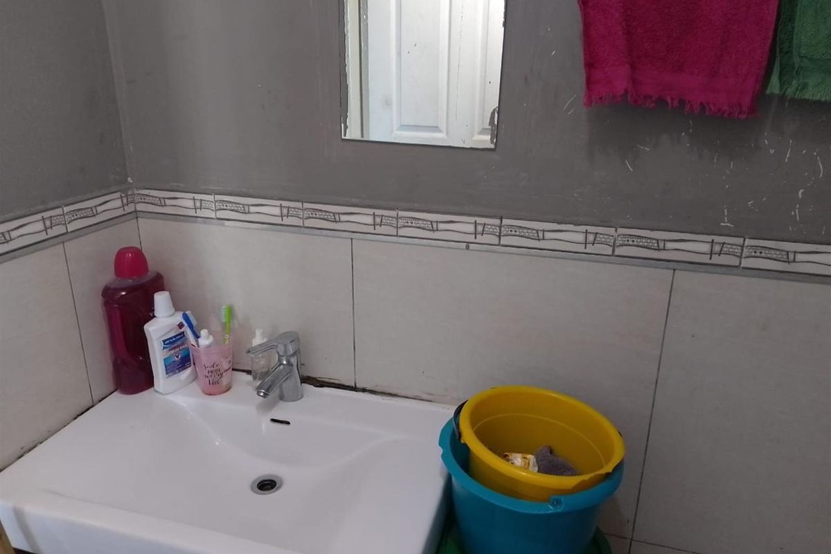 A functional bathroom vanity area featuring a wall-mounted basin, chrome mixer tap, and tiled splashback, currently showing signs of wear on the wall surfaces.