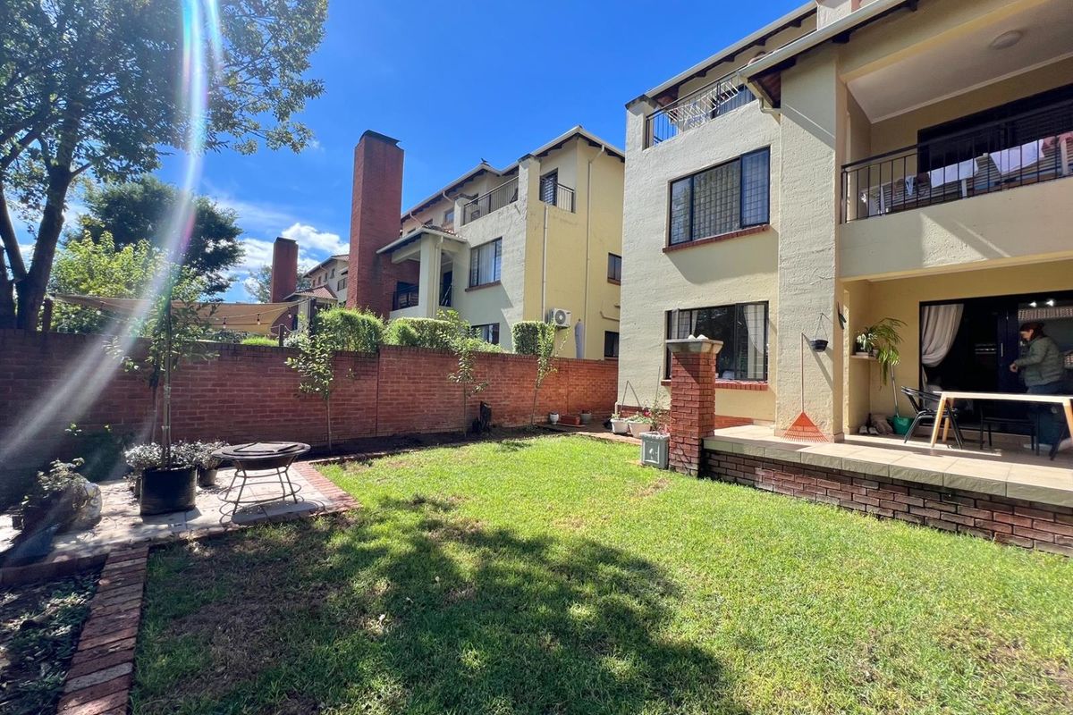 A private rear garden featuring a paved patio area, brick boundary wall, and established lawn, providing outdoor space for the apartment unit.