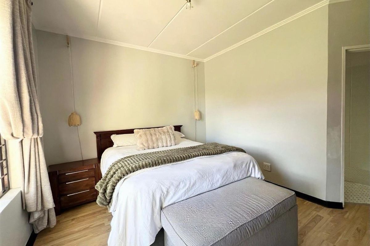 A well-lit bedroom featuring light wood-look flooring, crown molding, and an en-suite bathroom entrance.