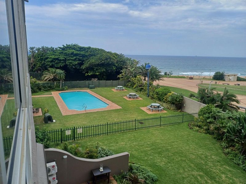 Elevated view of the communal swimming pool, landscaped garden, and direct ocean views from the apartment balcony.