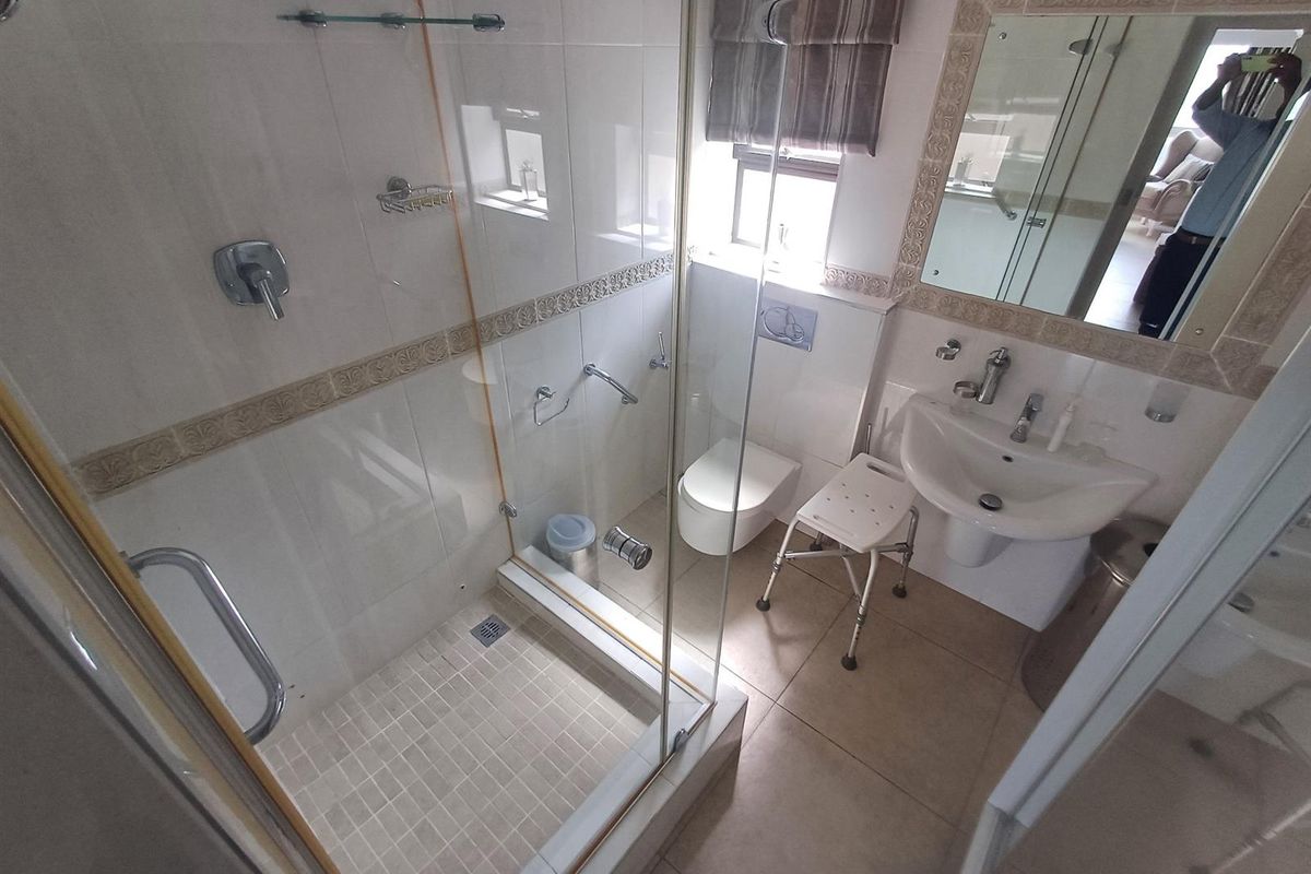 Compact bathroom featuring a glass-enclosed shower, wall-mounted toilet, and pedestal basin with decorative tile accents.