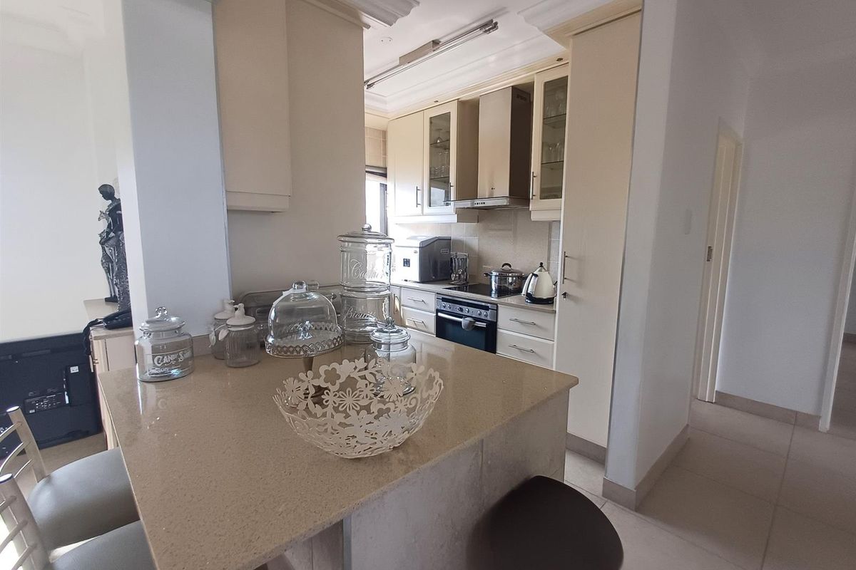 A functional kitchen featuring light-toned cabinetry, stone countertops, a breakfast bar, and integrated stainless steel appliances including an oven and extractor fan.