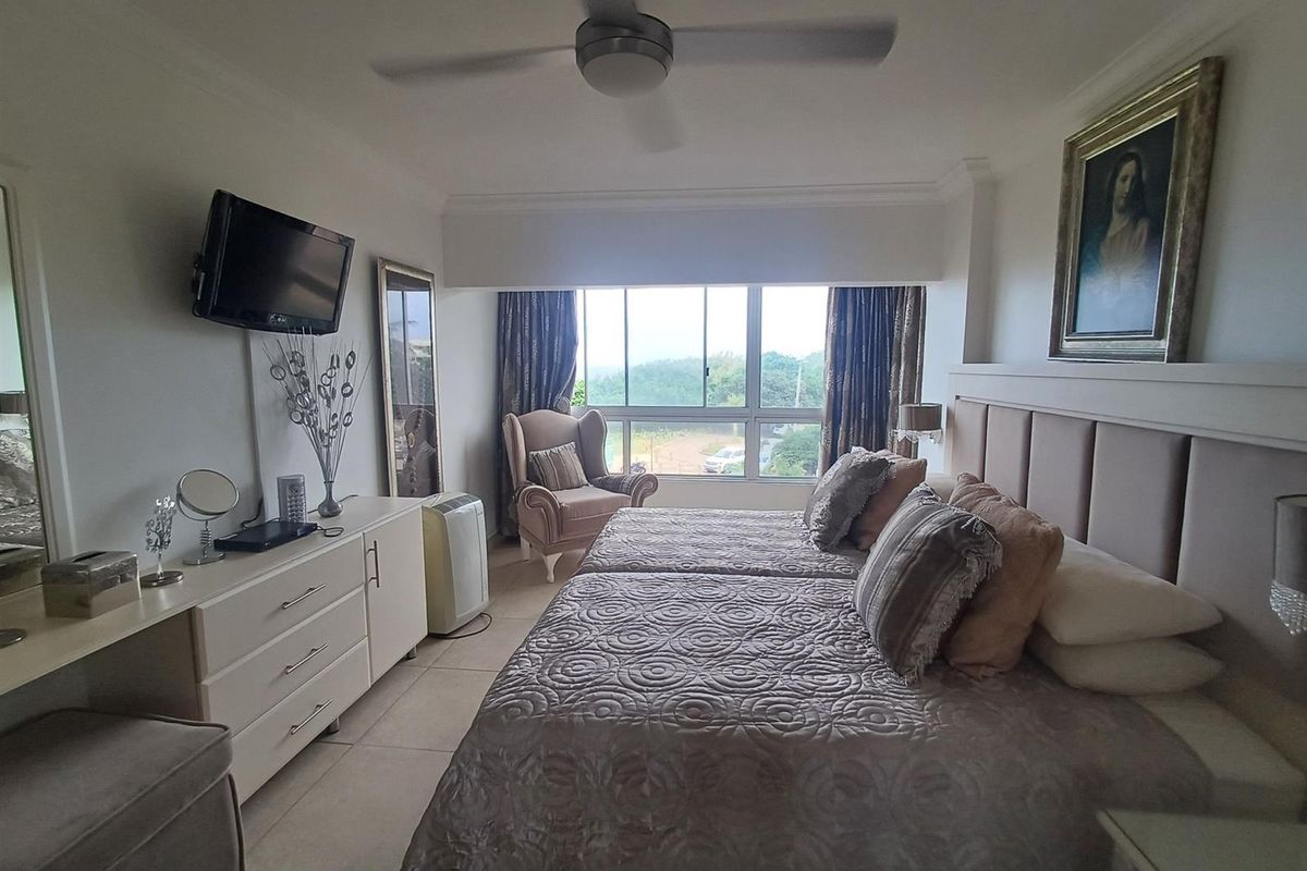 A well-lit bedroom featuring a large window with exterior views, a ceiling fan, and a neutral tiled floor.
