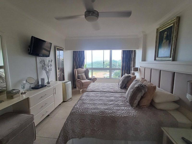 A well-lit bedroom featuring a large window with exterior views, a ceiling fan, and a neutral tiled floor.