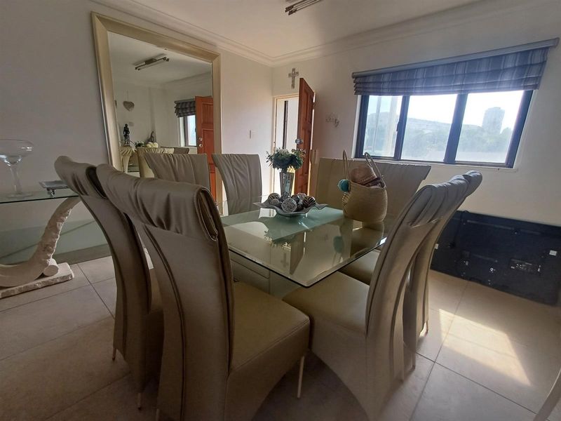 A bright dining room featuring tiled flooring, a large wall-mounted mirror, and a window with a fitted roman blind.