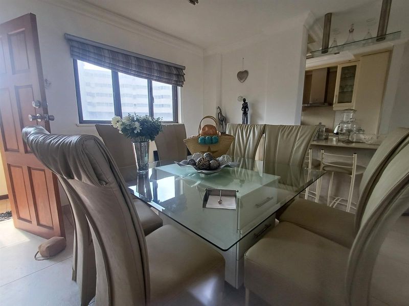 Open-plan dining area adjacent to a functional kitchen, featuring tiled flooring and a window with a roller blind.
