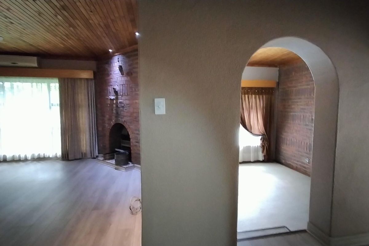 Spacious living area featuring a brick fireplace, timber-clad ceiling, and an arched entryway connecting to an adjacent room.