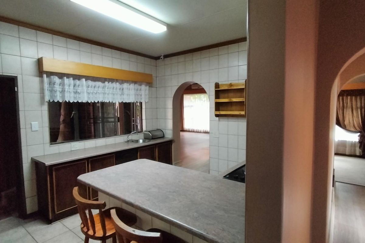 A dated kitchen featuring tiled walls, laminate countertops, and built-in cabinetry, connected to adjacent living spaces via an architectural archway.
