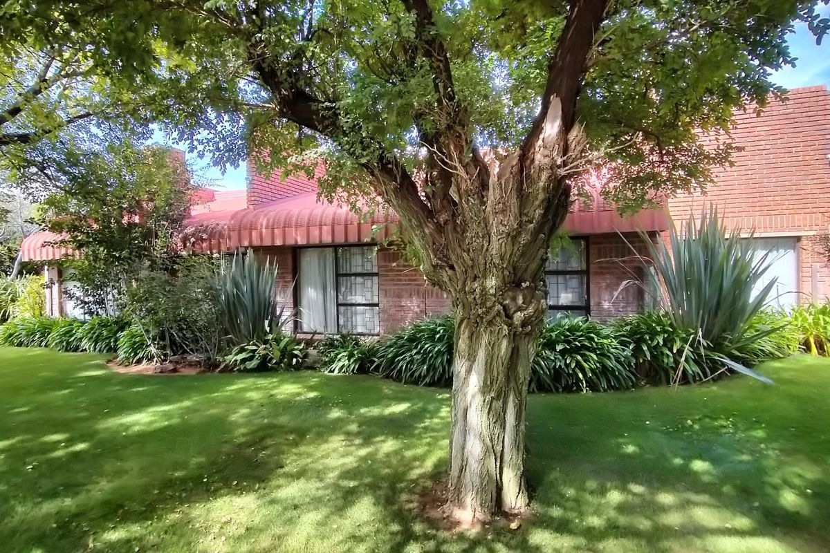 A view of the rear brick facade featuring red metal awnings, large windows, and a well-maintained garden with mature trees.