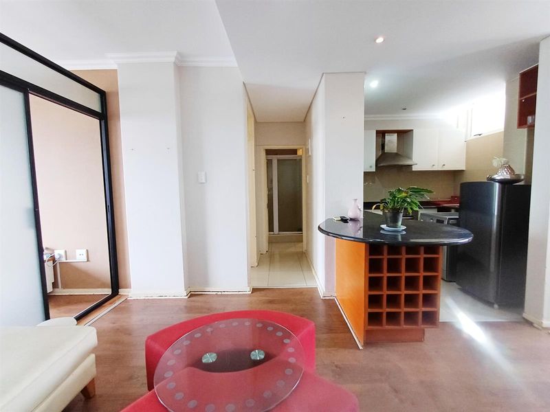 Open-plan living area featuring laminate flooring, a kitchen with granite countertops, built-in cabinetry, and a wine rack, leading to a hallway.