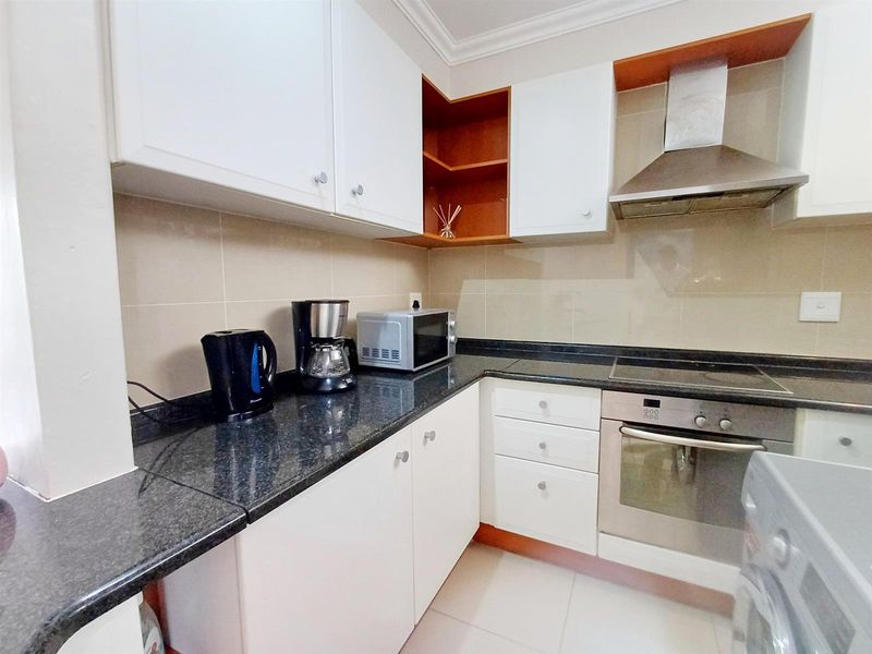 A functional kitchen featuring white cabinetry, dark granite countertops, a built-in oven, electric hob, and stainless steel extractor fan.