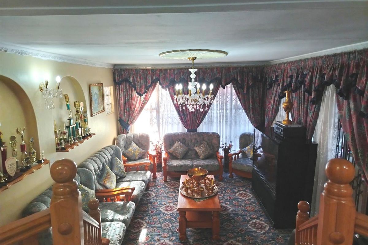 A traditional living room featuring a crystal chandelier, decorative ceiling rose, wall niches, and a wooden staircase balustrade.