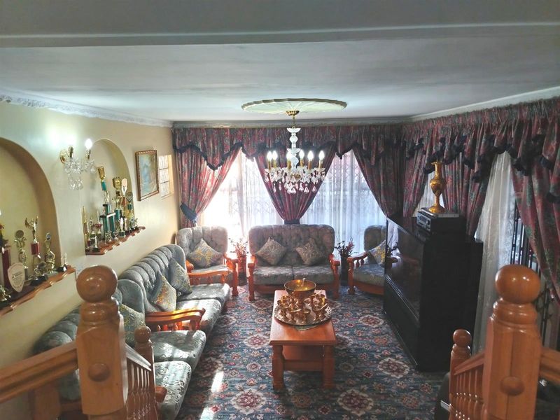 A traditional living room featuring a crystal chandelier, decorative ceiling rose, wall niches, and a wooden staircase balustrade.