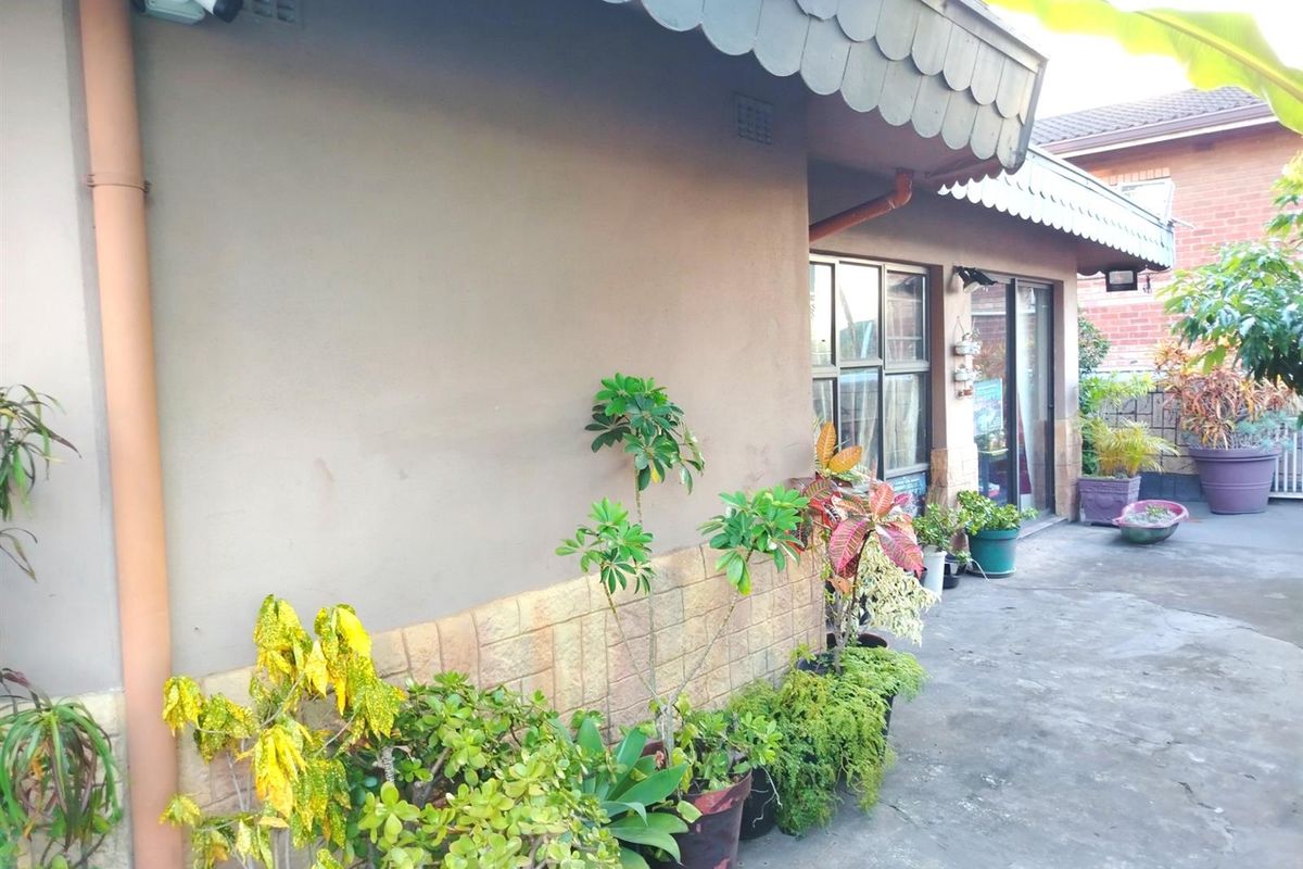A rear exterior view of the property featuring a concrete patio area, sliding glass doors, and a security camera mounted on the wall.