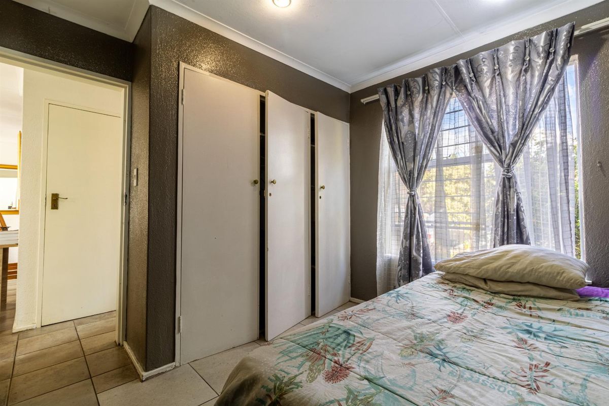 A bedroom featuring built-in cupboards, tiled flooring, and a window with security bars, providing a functional living space.