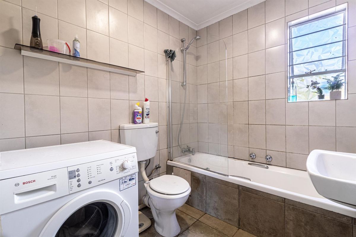 A functional bathroom featuring a bathtub with a glass shower screen, a toilet, and a dedicated space for a washing machine.