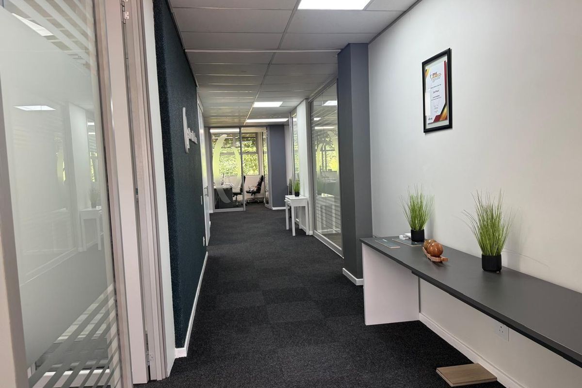 A professional commercial office hallway featuring carpeted flooring, glass-partitioned office doors, and a built-in wall-mounted console desk.