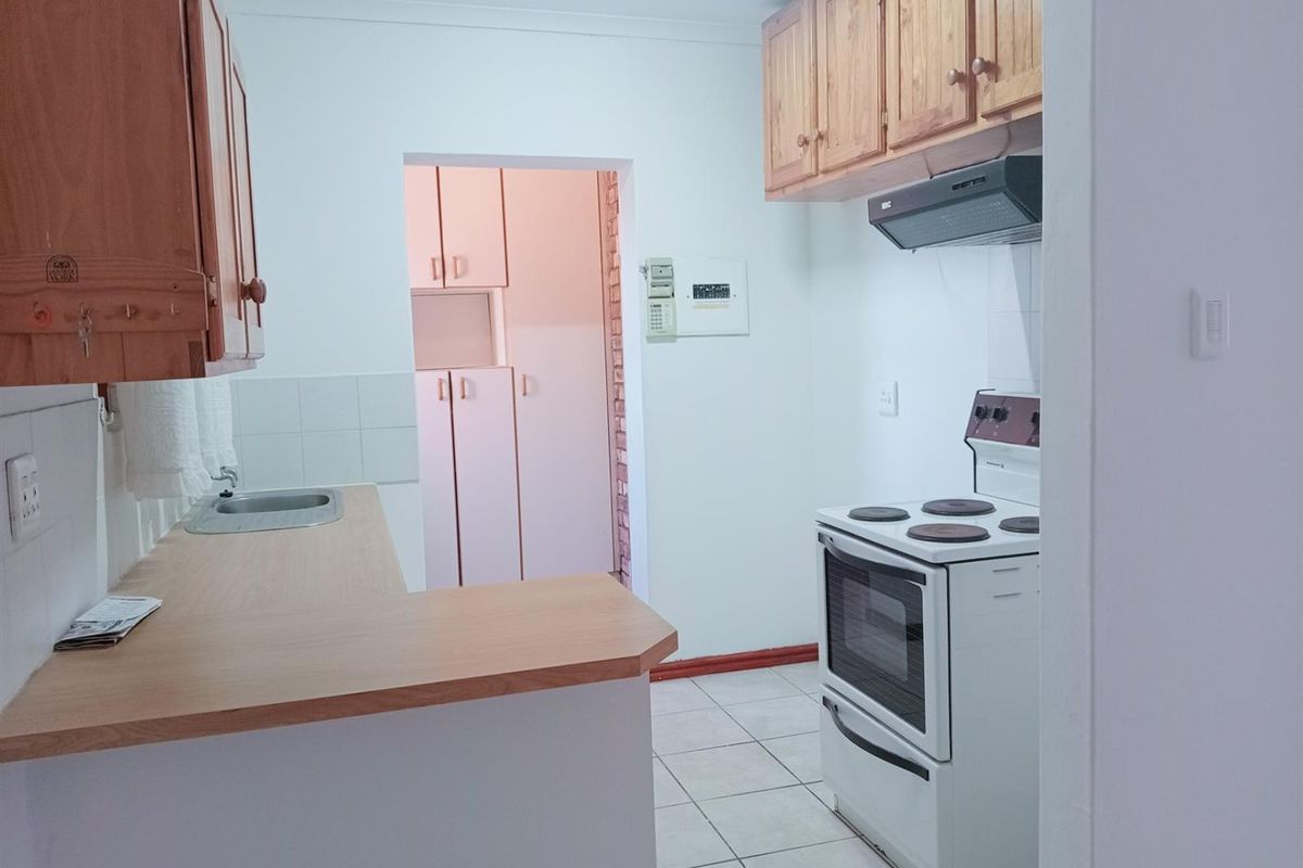 A functional kitchen featuring wooden cabinetry, a built-in stove with extractor fan, and tiled flooring, with an adjacent scullery area.