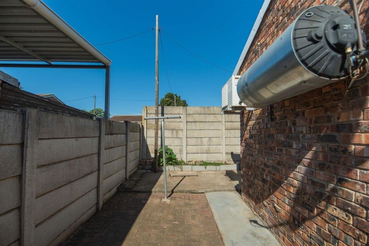 A functional rear exterior area featuring a brick wall, concrete and paved flooring, and an externally mounted hot water cylinder.