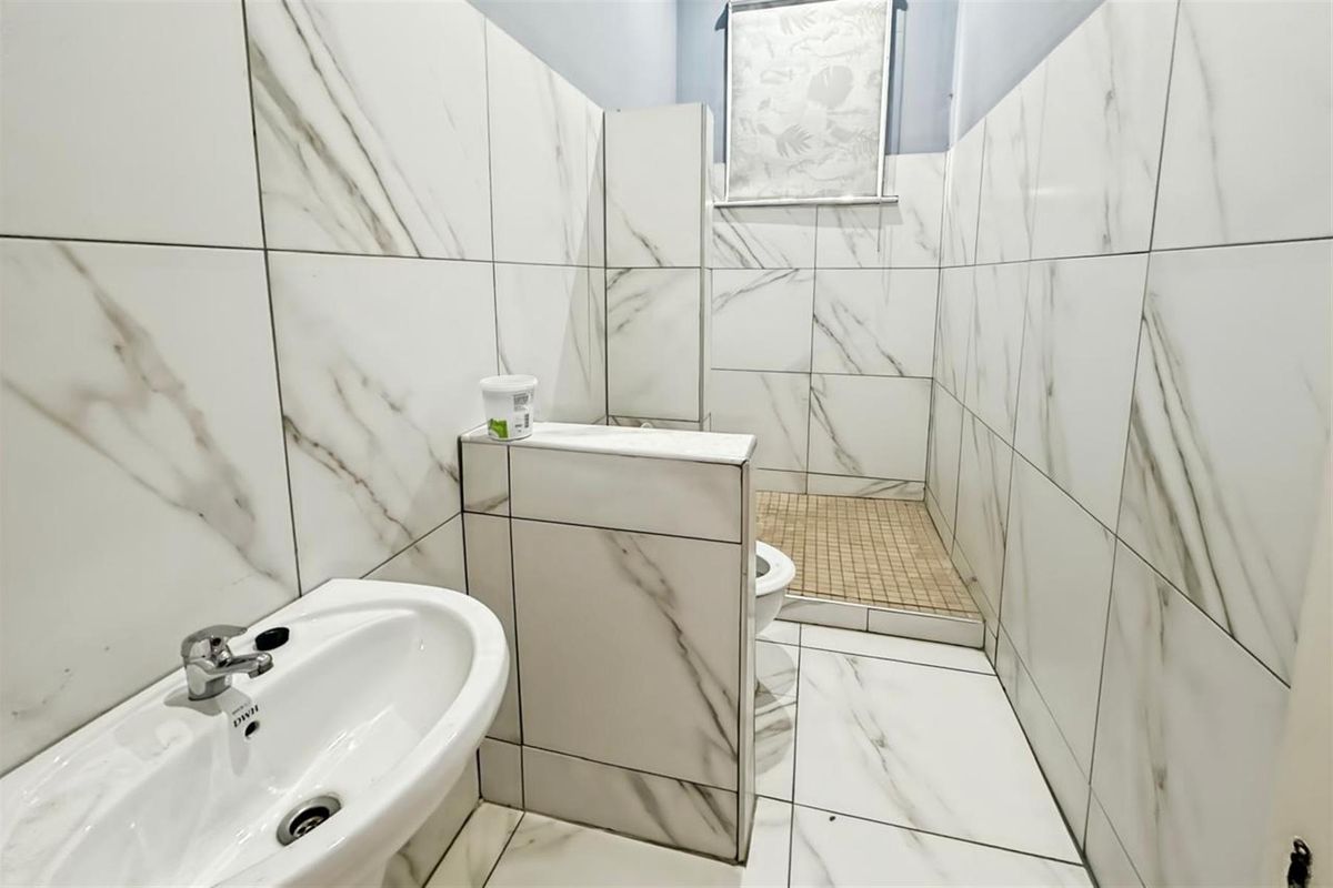 A modern bathroom featuring floor-to-ceiling marble-look wall tiles, a pedestal basin, and a walk-in shower enclosure with mosaic floor tiling.