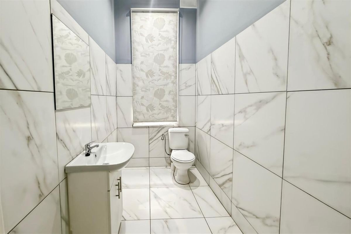 A modern bathroom featuring floor-to-ceiling marble-look wall tiles, tiled flooring, a wall-mounted mirror, and a white vanity basin with a toilet.