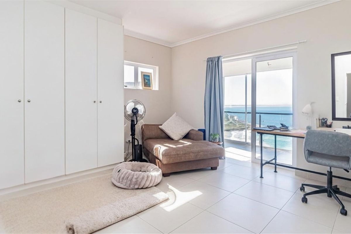 Bright bedroom featuring built-in cupboards, tiled flooring, and sliding glass doors opening to a balcony with scenic ocean views.