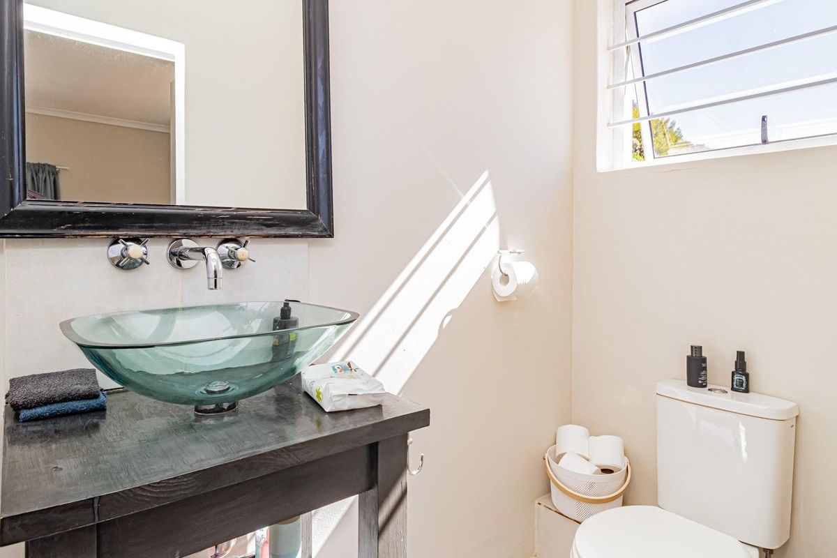 A bright bathroom featuring a modern glass vessel sink, wall-mounted faucet, dark wood vanity, and a functional toilet under a top-hung window.