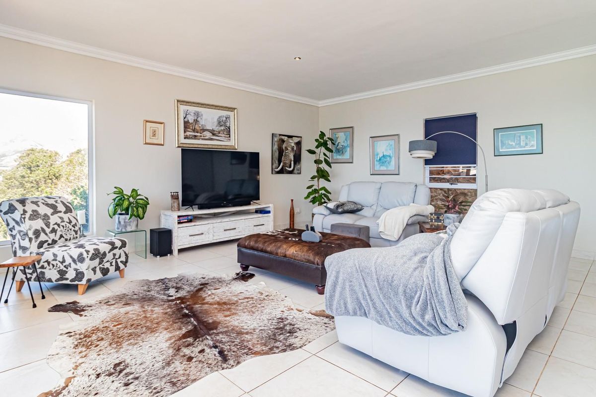 A bright and spacious living room featuring neutral tiled flooring, recessed lighting, and a large window providing natural light.