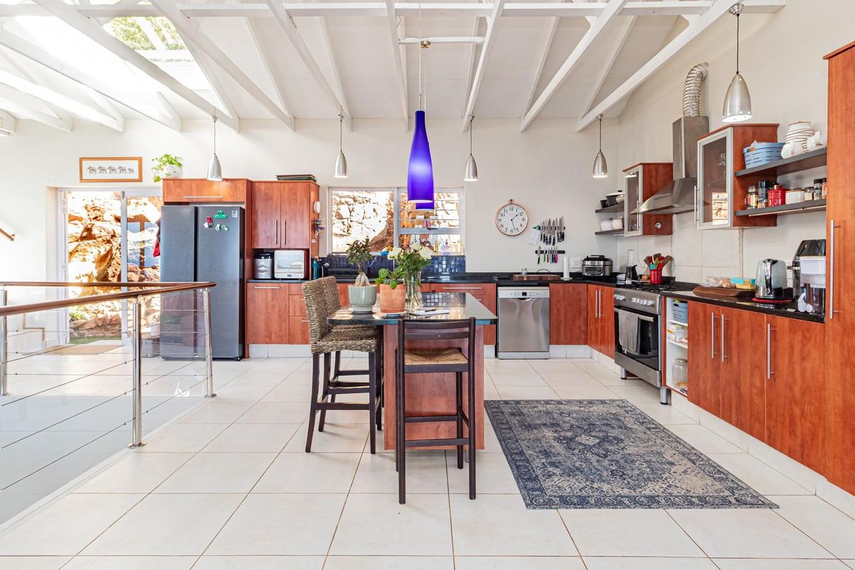 Spacious open-plan kitchen featuring warm wooden cabinetry, a central island with seating, stainless steel appliances, and high ceilings with exposed white beams.