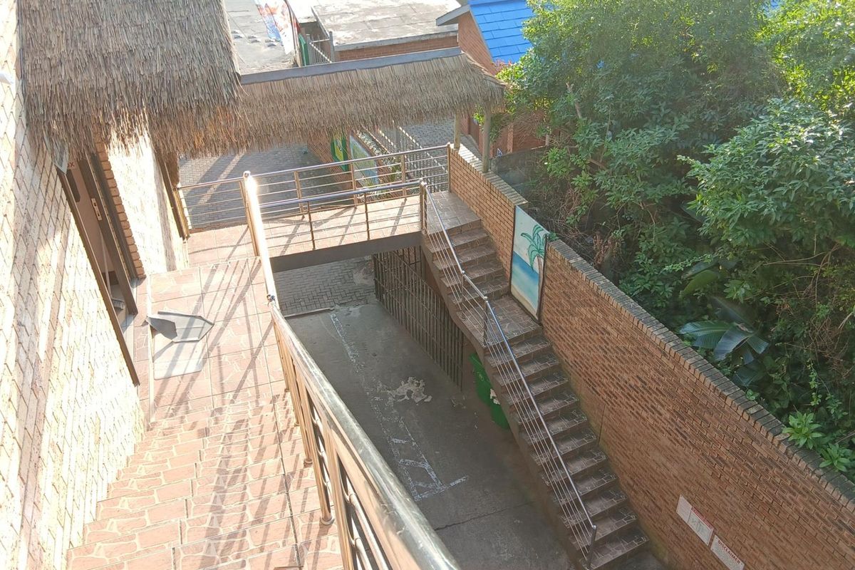 An elevated view of an outdoor staircase and walkway featuring brick construction, stainless steel railings, and a thatched roof covering.