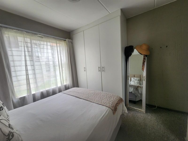 A functional bedroom featuring built-in cupboards, carpeted flooring, and large windows with security bars, offering a neutral canvas for personalization.