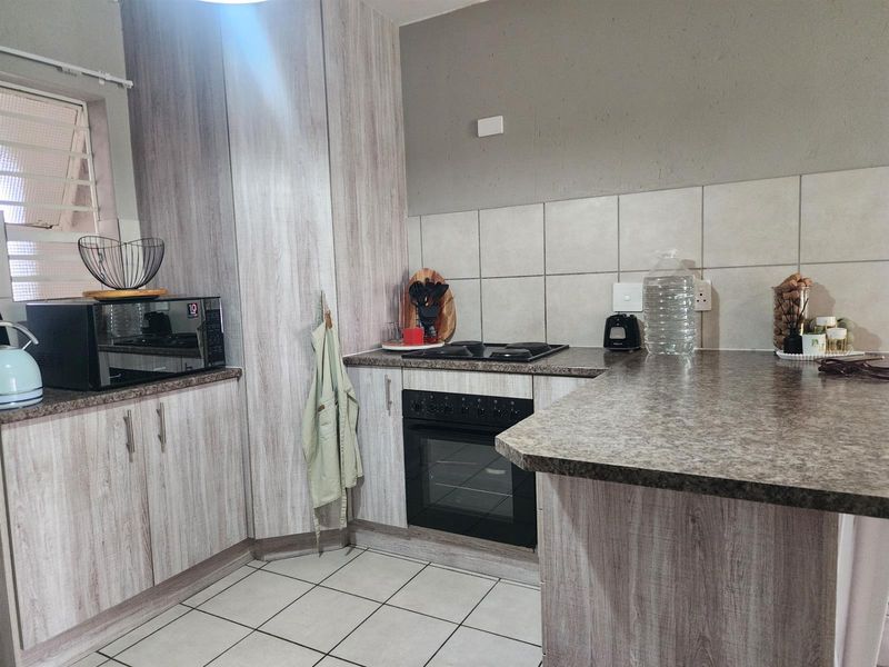 A functional kitchen featuring light wood-grain cabinetry, laminate countertops, a built-in oven and hob, and tiled flooring with a neutral backsplash.