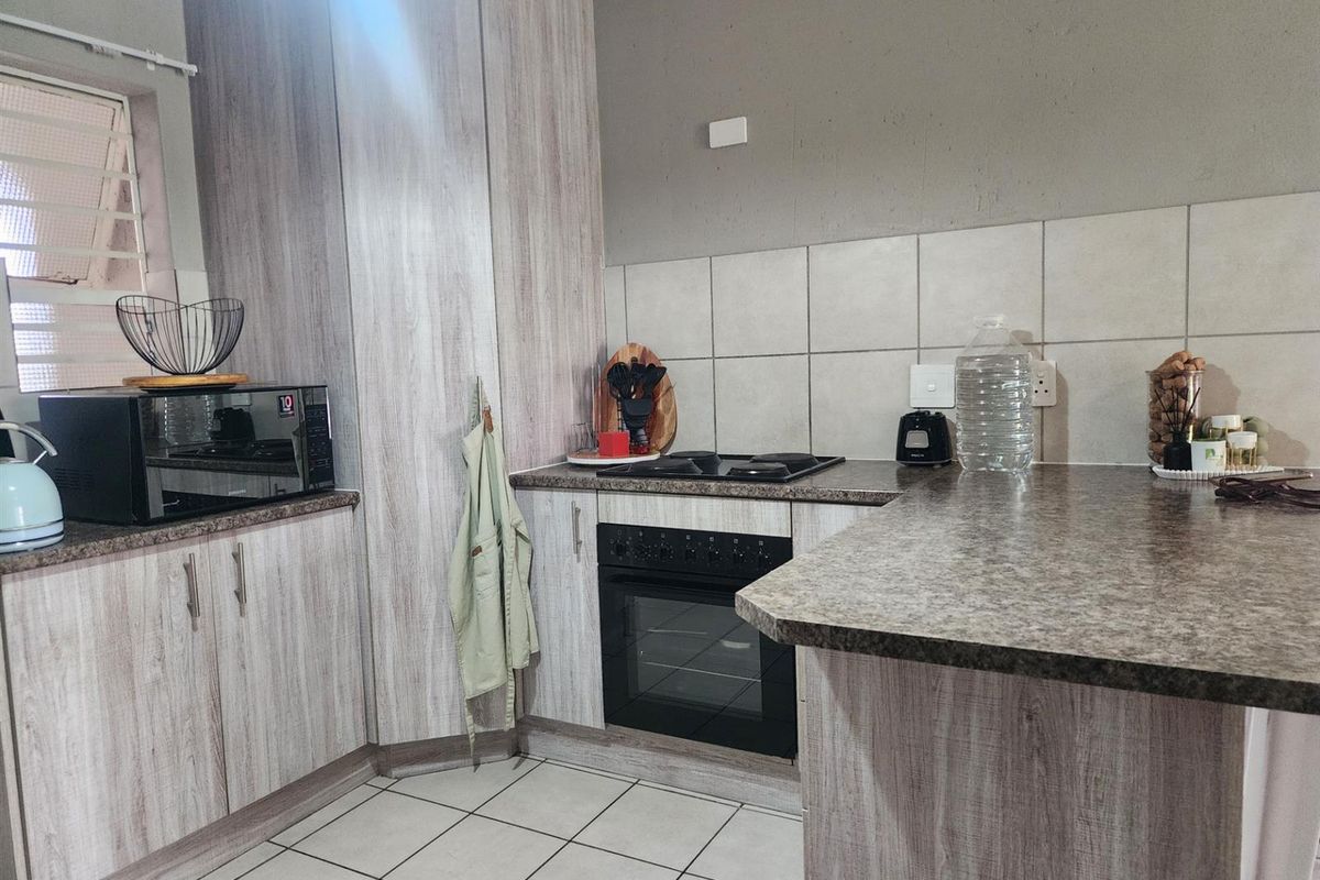A functional kitchen featuring light wood-grain cabinetry, laminate countertops, a built-in oven and hob, and tiled flooring with a neutral backsplash.