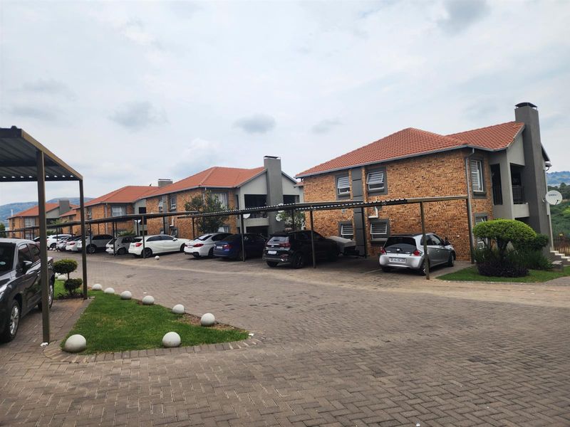 Exterior view of a multi-unit apartment complex featuring face brick facades, tiled roofs, and covered carport parking bays.