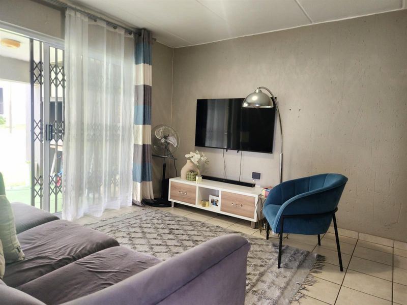 A living room featuring tiled flooring and a sliding glass door with a security gate, providing access to an outdoor area.