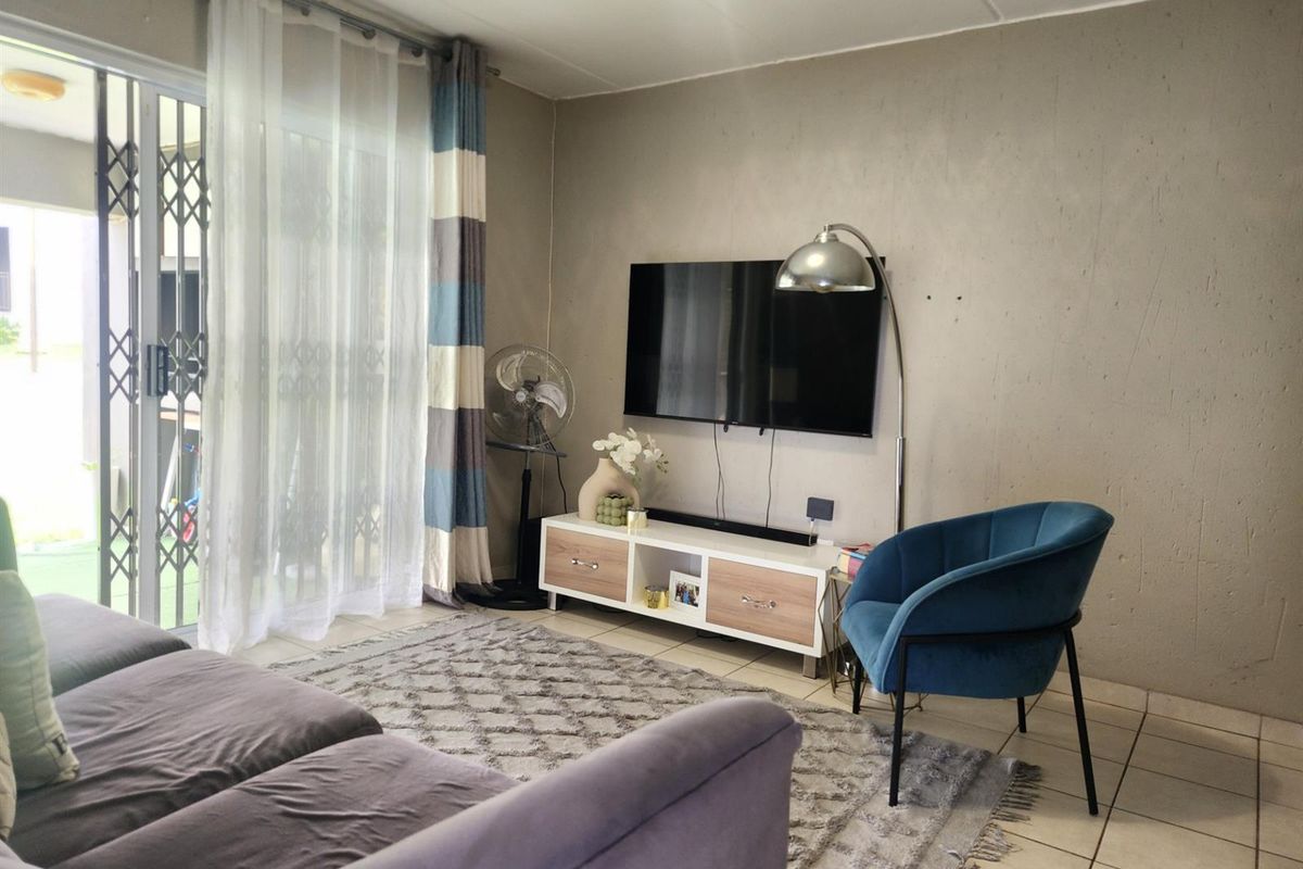 A living room featuring tiled flooring and a sliding glass door with a security gate, providing access to an outdoor area.