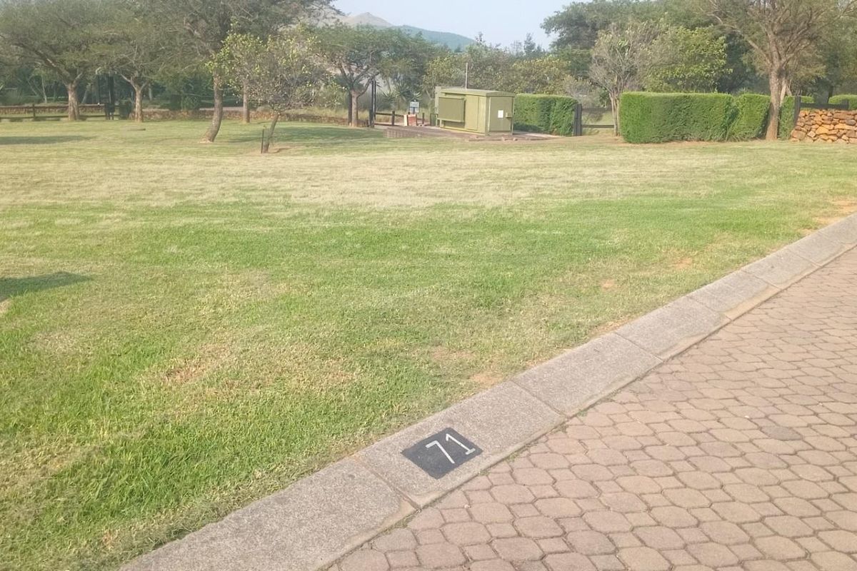 A view of a vacant residential plot featuring well-maintained grass, paved street access, and established perimeter landscaping.