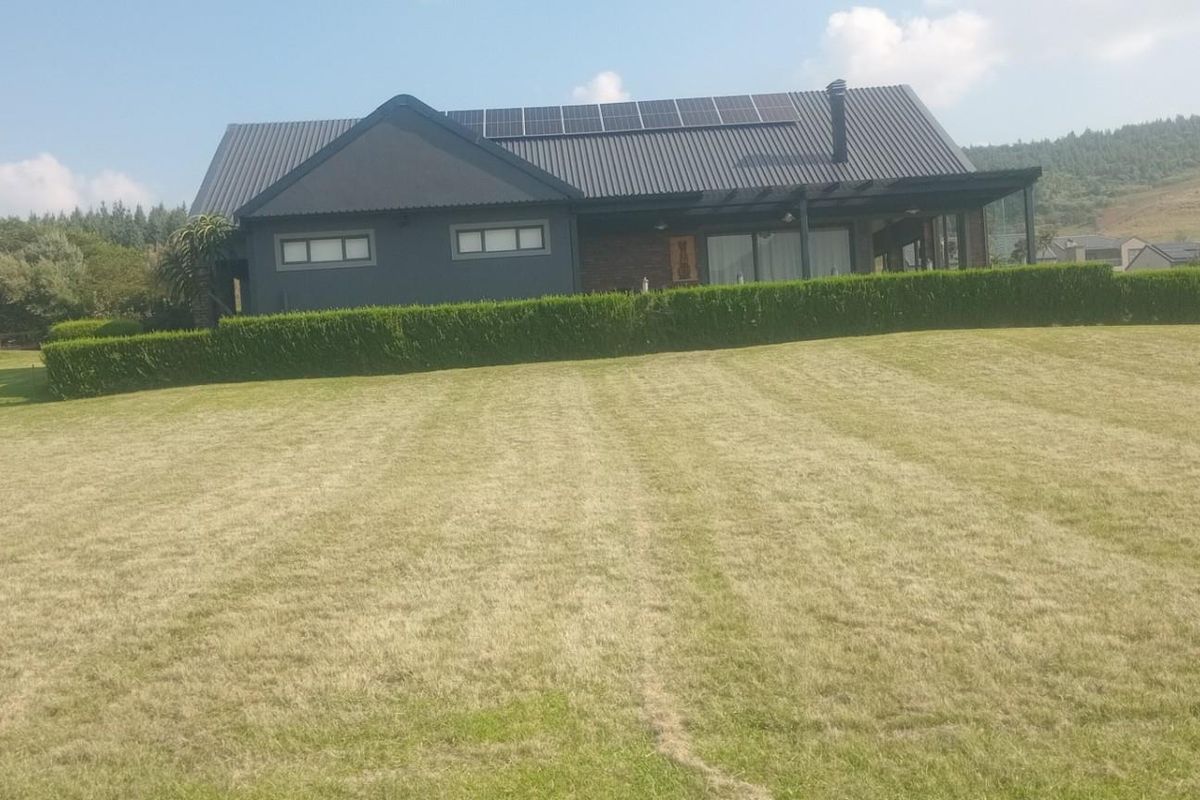 A view of the rear exterior of a modern residential property featuring a dark metal roof, solar panels, and a well-maintained lawn.