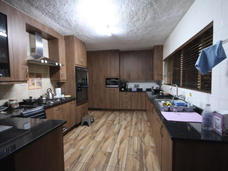 Spacious kitchen featuring wood-finish cabinetry, granite countertops, built-in oven, extractor fan, and durable tiled flooring with ample storage space.