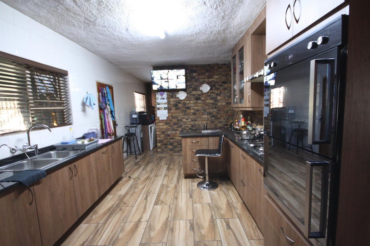 A functional kitchen featuring wood-look cabinetry, granite countertops, a built-in oven, and a distinctive exposed brick feature wall.