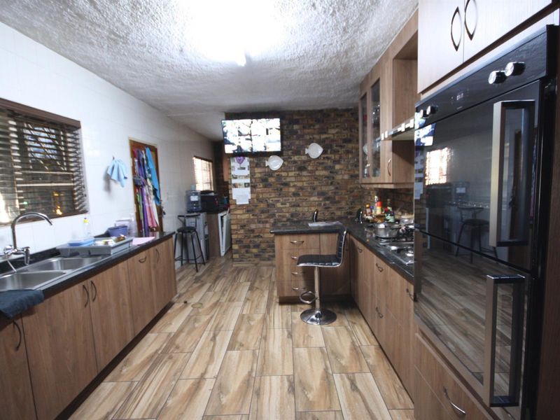 A functional kitchen featuring wood-look cabinetry, granite countertops, a built-in oven, and a distinctive exposed brick feature wall.