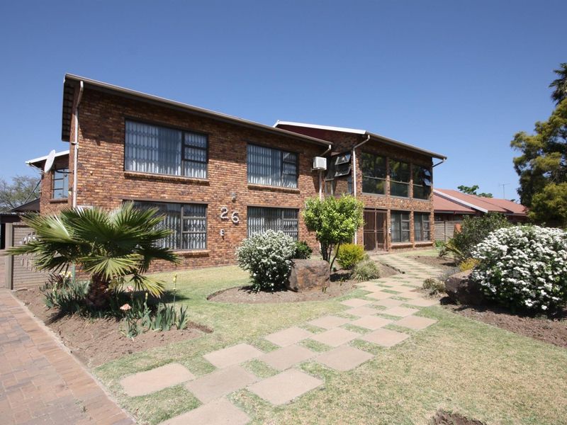 A well-maintained two-story face brick residential building featuring a paved walkway, established garden, and secure window treatments.