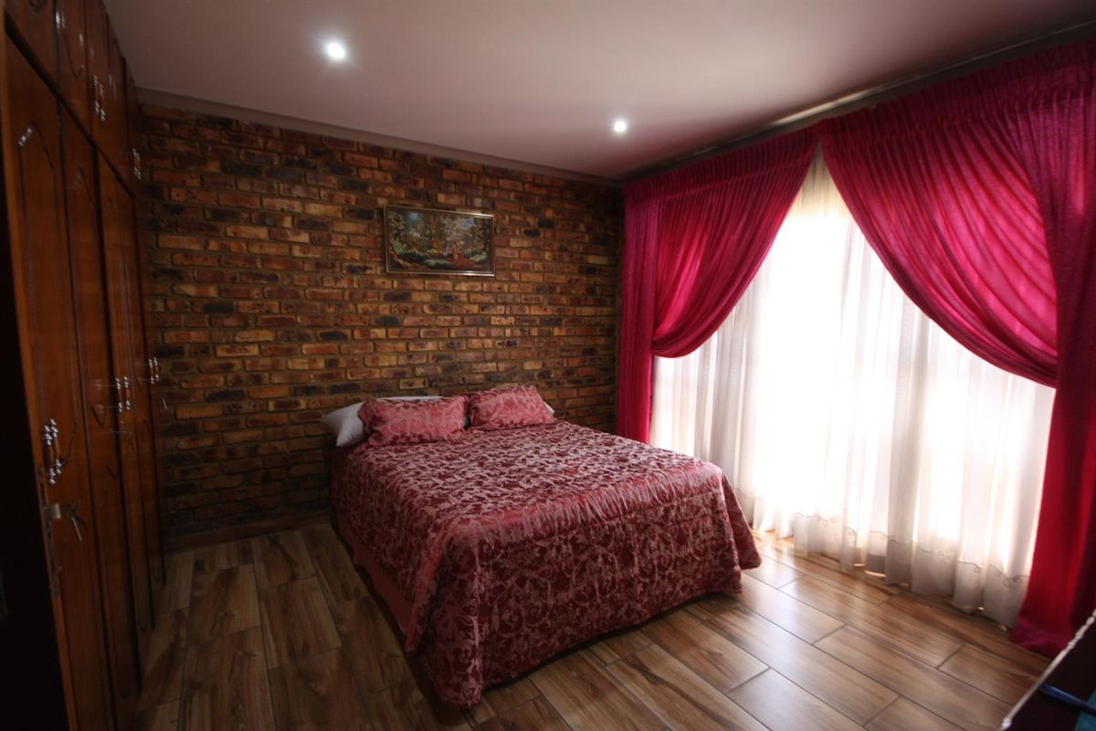 A well-maintained bedroom featuring an exposed brick accent wall, built-in wooden cabinetry, and modern wood-look tile flooring with recessed ceiling lighting.