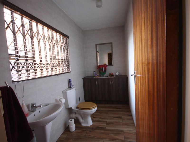 A functional bathroom featuring tiled walls and flooring, a pedestal basin, a toilet, and a built-in vanity cabinet for storage.