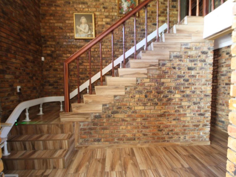 An inviting entrance hall featuring a striking exposed brick wall, a wooden staircase with a matching balustrade, and modern laminate flooring.