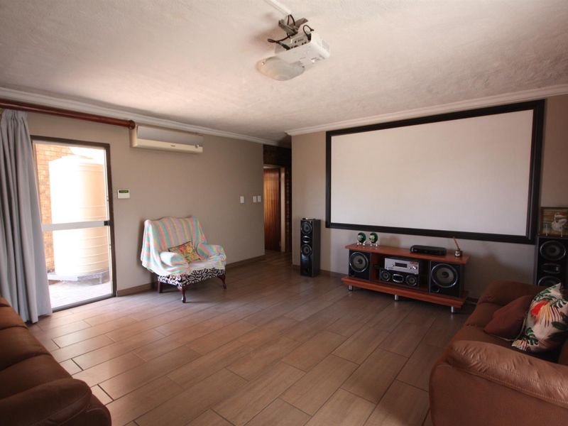 A dedicated cinema room featuring a large wall-mounted projection screen, ceiling-mounted projector, tiled flooring, and direct access to an outdoor area.