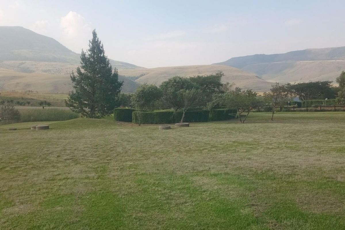 A scenic view of a well-maintained grassy landscape featuring mature trees, manicured hedges, and distant rolling hills.