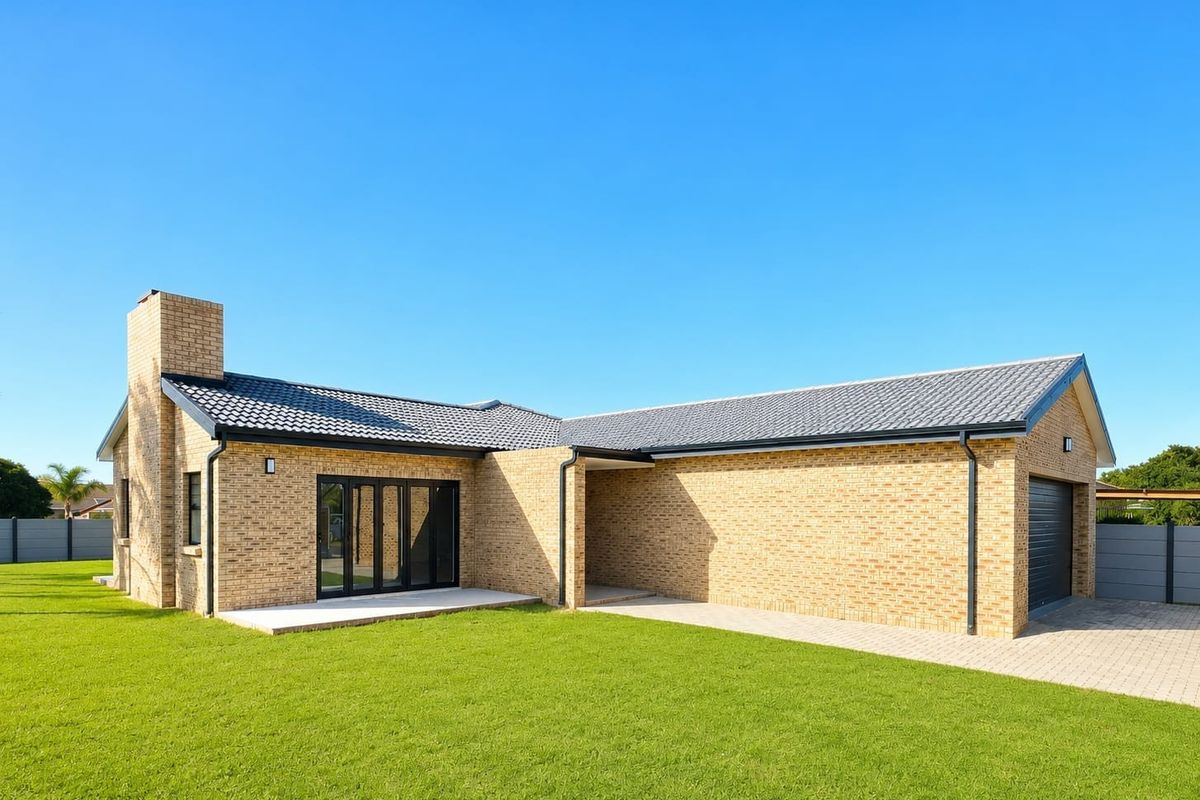 Rear view of a modern single-story brick house featuring a tiled roof, integrated garage, paved driveway, and a small concrete patio area.
