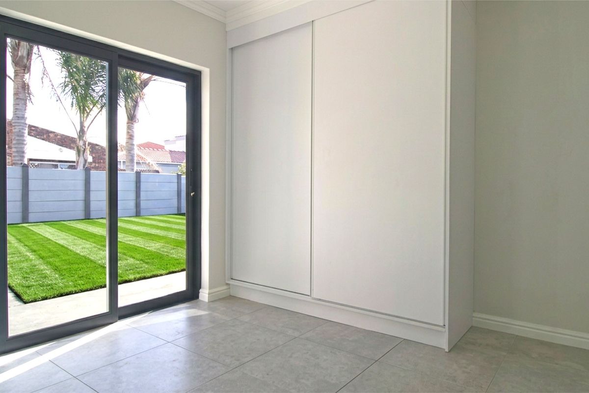 A bright, modern bedroom featuring neutral tiled flooring, a large built-in sliding wardrobe, and direct access to the rear garden through sliding glass doors.